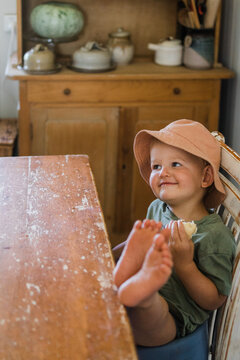 male toddler looks cheekily out of frame with his feet on a table