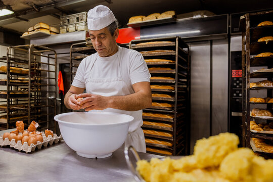 Mature baker breaking eggs for pastry