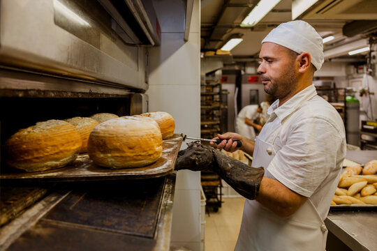 Male baker checking bread in oven