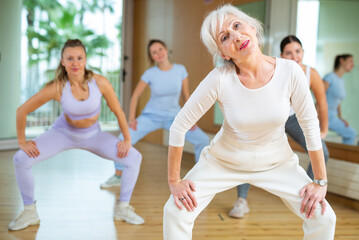 Practiced old-aged woman engaging in aerobics in dance studio during workout session. Women...