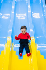 Happy, smiling little boy, preschool child descends, slides down a plastic slide on an indoor playground. Photography, childhood and emotions concept.