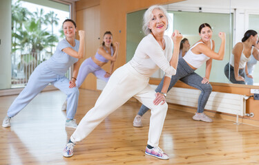 Active positive senior woman performing dance elements during lesson with female group in modern school for adults