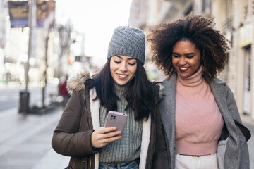 Cheerful multiethnic friends using smartphone in the city