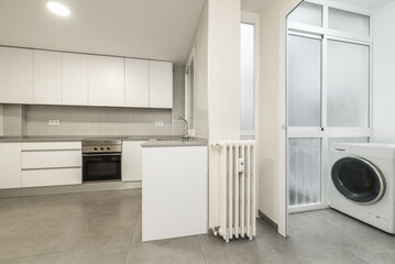Kitchen furnished with white furniture without handles, washing machine on the terrace, cast iron...