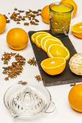 A still life with glass juicer, sliced oranges, cut glass vase filled with fresh orange juice surrounded by slices and whole oranges