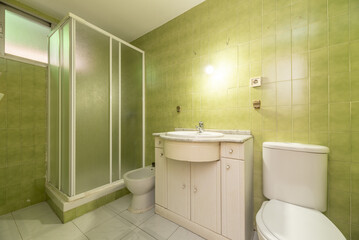 conventional bathroom with white furniture and shower cabin with sliding screens with white aluminum edges and green tiles