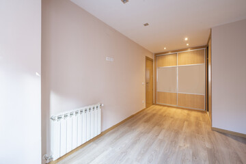 Empty room with light pink walls with a built-in wardrobe with sliding oak doors and tempered glass