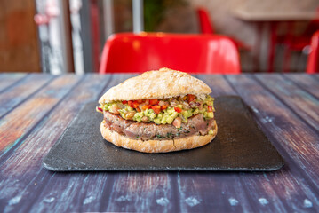 A tuna burger with pico de gallo and guacamole served on a black slate