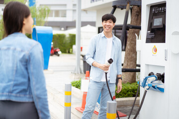 Fototapeta premium Asian man and woman holding AC type 2 EV charging connector at EV charging station. Road vehicle traveling or transportation with the clean energy concept.