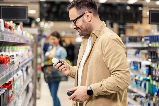 A man standing in supermarket next to an aisle and choosing deodorant.