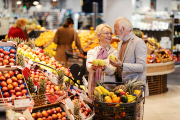 A happy senior couple is choosing fresh fruits at the supermarket and smiling at each other.