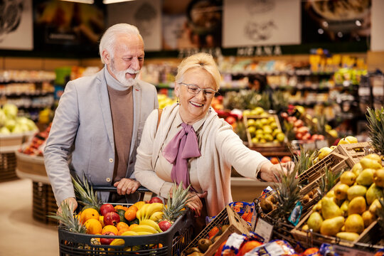 A cheerful senior couple is purchasing fresh, healthy groceries at the supermarket. Couple is buying fruits.