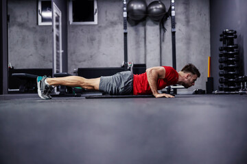 Strength and perseverance. A handsome and attractive man does demanding exercises for the arms and shoulders. He is in a plank position and does push-ups. Discipline and good feeling. Copy space