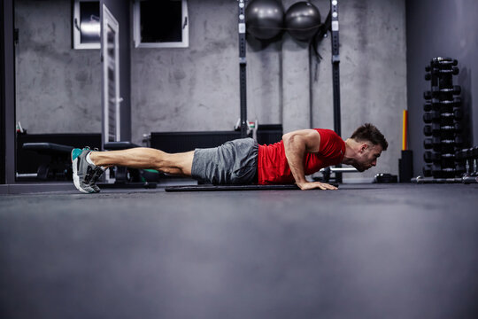 Strength and perseverance. A handsome and attractive man does demanding exercises for the arms and shoulders. He is in a plank position and does push-ups. Discipline and good feeling. Copy space