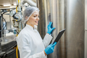 A dairy factory worker is checking on milk processing machine and smiling at the tablet.