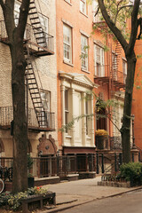stone building with balconies and fire escape ladders near trees on sidewalk in New York City.