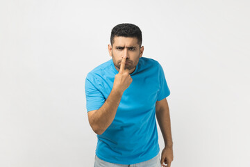 Portrait of unshaven man wearing blue T- shirt looking with incredulous suspicious gaze and...