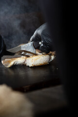 A view of a chef slicing raw chicken breast on the griddle surface of a restaurant kitchen.