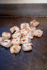 A view of raw shrimp cooking on a griddle surface of a restaurant kitchen.