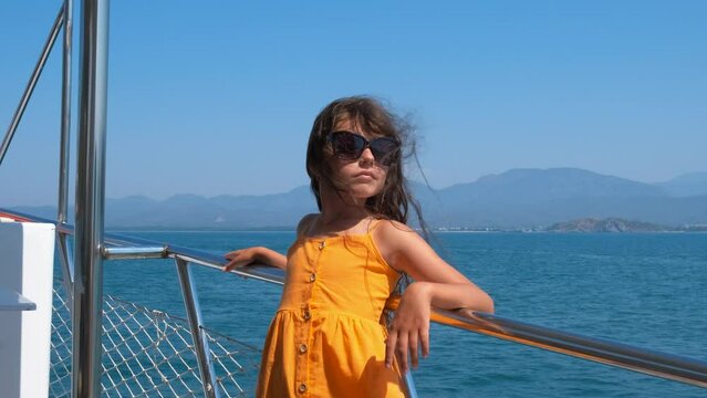 Child enjoy wind on yacht. A cute playful ittle girl in sunglasses enjoy the sea waves from the yacht. A concept of windy time and sea travel in summer.