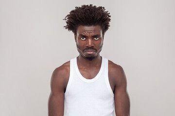 Sad unhappy man with Afro hairstyle frowning face, being upset with bad news he received, looking at camera with pout lips, wearing white T-shirt. Indoor studio shot isolated on gray background.