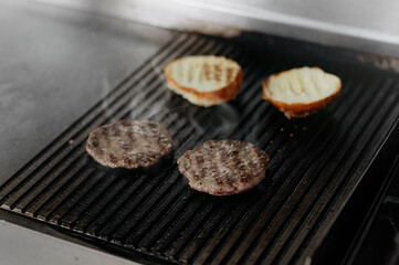 Chef cooking pieces of meat, buns, cutlet for burgers on grill. close up view. the process of making a burger