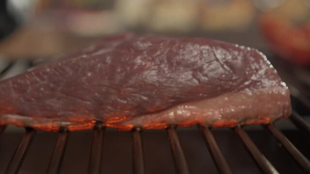 Whole picanha roasting on the grill with strong fire and flames.