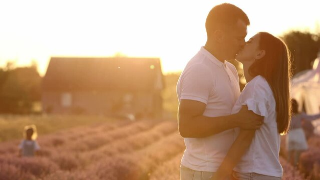 Young heterosexual couple in love are gently kissing and hugging in a blooming lavender field in sunlights. Love story of happy man and woman in nature on sunset. Romantic atmosphere, true feelings