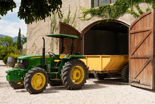 Robertson, Western Cape South Africa. 2023.  Green tractor with yellow wheels and trailer halfway  in  a large barn.
