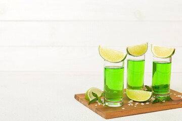 Sweet refreshing mint liqueur, with ice and mint leaves on table background, Shots with lime slice and mint flat lay