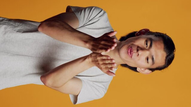Vertical video: Male model blowing air kisses in studio, acting silly and sensual on orange backdrop. Carefree man sending kisses and being flirty, acting romantic with kissy funny face. Natural