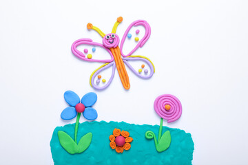 Butterfly and flowers made of plasticine on white background, top view