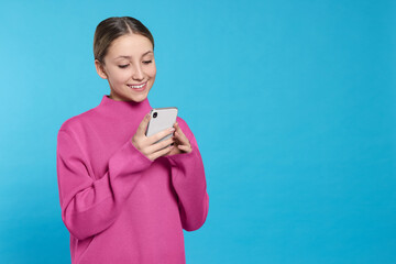 Teenage girl using smartphone on light blue background. Space for text