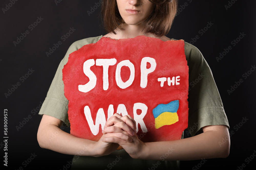 Wall mural sad woman holding poster with words stop the war on black background, closeup