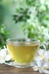 Cup of tea and fresh jasmine flowers on wooden table. Space for text