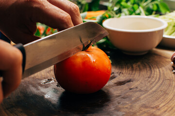 Tomato being sliced on a wooden board for an organic salad recipe