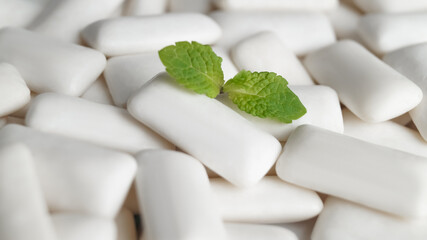 Tasty chewing gums and fresh mint leaves as background, closeup
