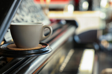 Cup with cork coaster on grand piano in cafe, closeup. Space for text