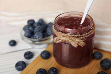 Jar of delicious blueberry jam and fresh berries on white table, closeup. Space for text