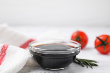 Bowl with balsamic vinegar, rosemary and tomatoes on white wooden table, closeup
