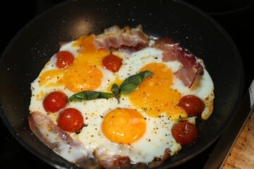 Tasty eggs with tomatoes and bacon in frying pan for breakfast, closeup
