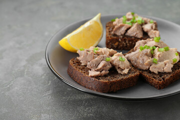 Tasty sandwiches with cod liver, lemon and green onion on light grey table