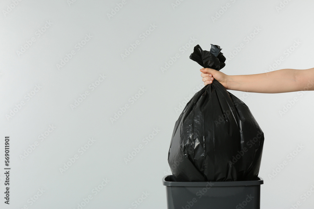 Poster Woman holding trash bag full of garbage over bucket on light grey background, closeup. Space for text