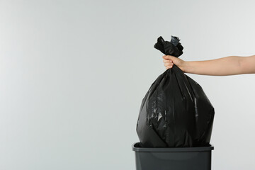 Woman holding trash bag full of garbage over bucket on light grey background, closeup. Space for...