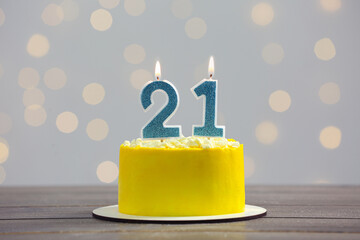 Coming of age party - 21st birthday. Delicious cake with number shaped candles on wooden table against blurred lights