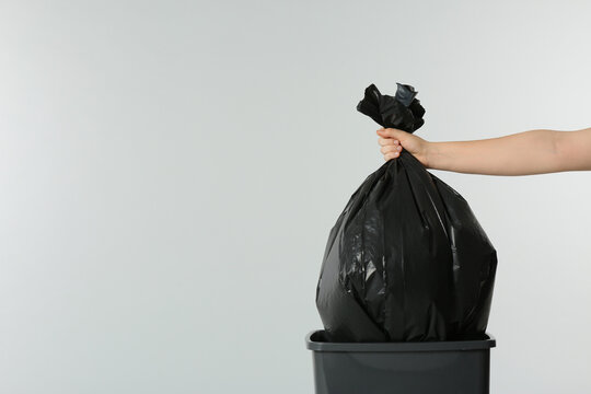 Woman holding trash bag full of garbage over bucket on light grey background, closeup. Space for text