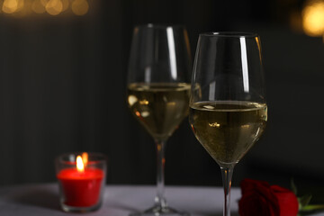 Glasses of white wine, burning candle and rose flower on table against blurred lights, space for text. Romantic atmosphere