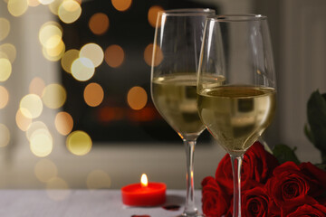Glasses of white wine, burning candle and rose flowers on grey table indoors, space for text. Romantic atmosphere