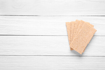 Fresh crunchy rye crispbreads on white wooden table, top view. Space for text