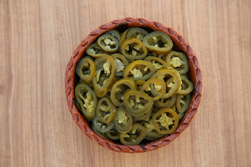 Pickled green jalapeno peppers on wooden table, top view